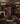 Wine cellar with shelves filled with bottles in a dimly lit room with chandeliers and a fireplace.